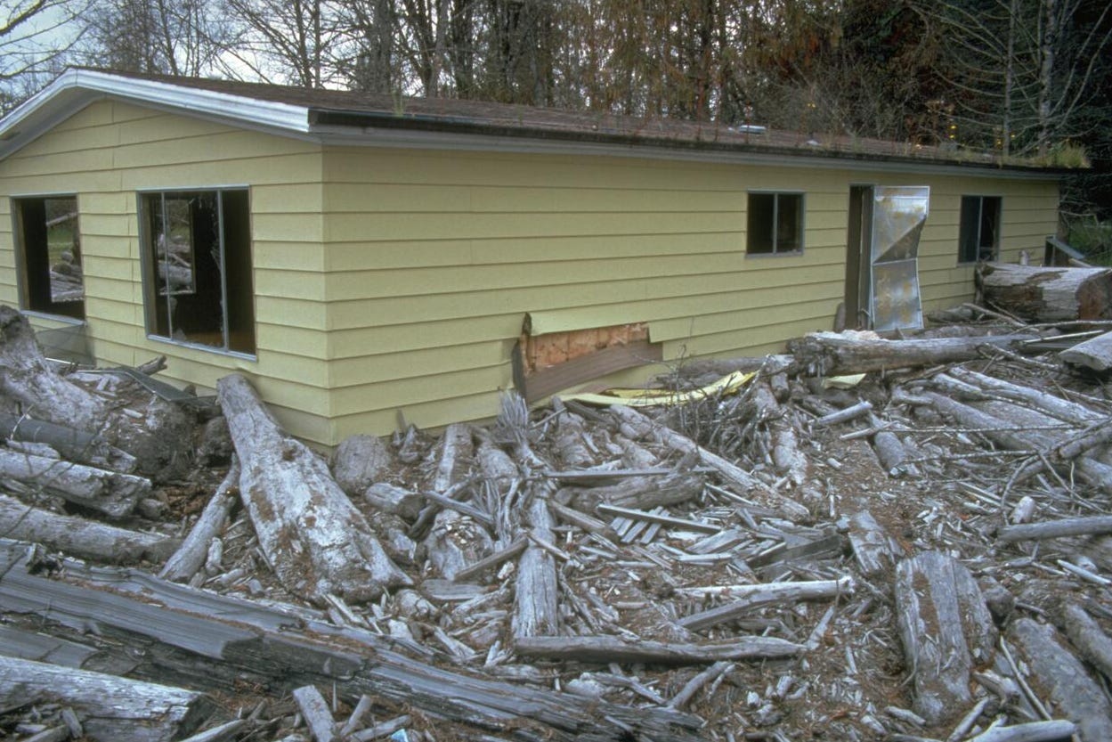 A yellow house is buried by broken trees and dirt