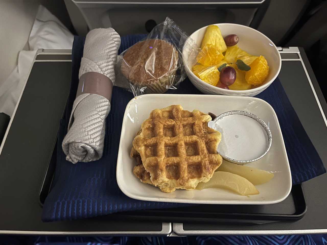 plate of waffles with fruit and a muffin on an airplane