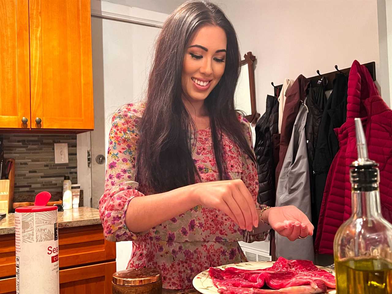 Lara, standing in her kitchen, sprinkles salt from her hand onto the steak.