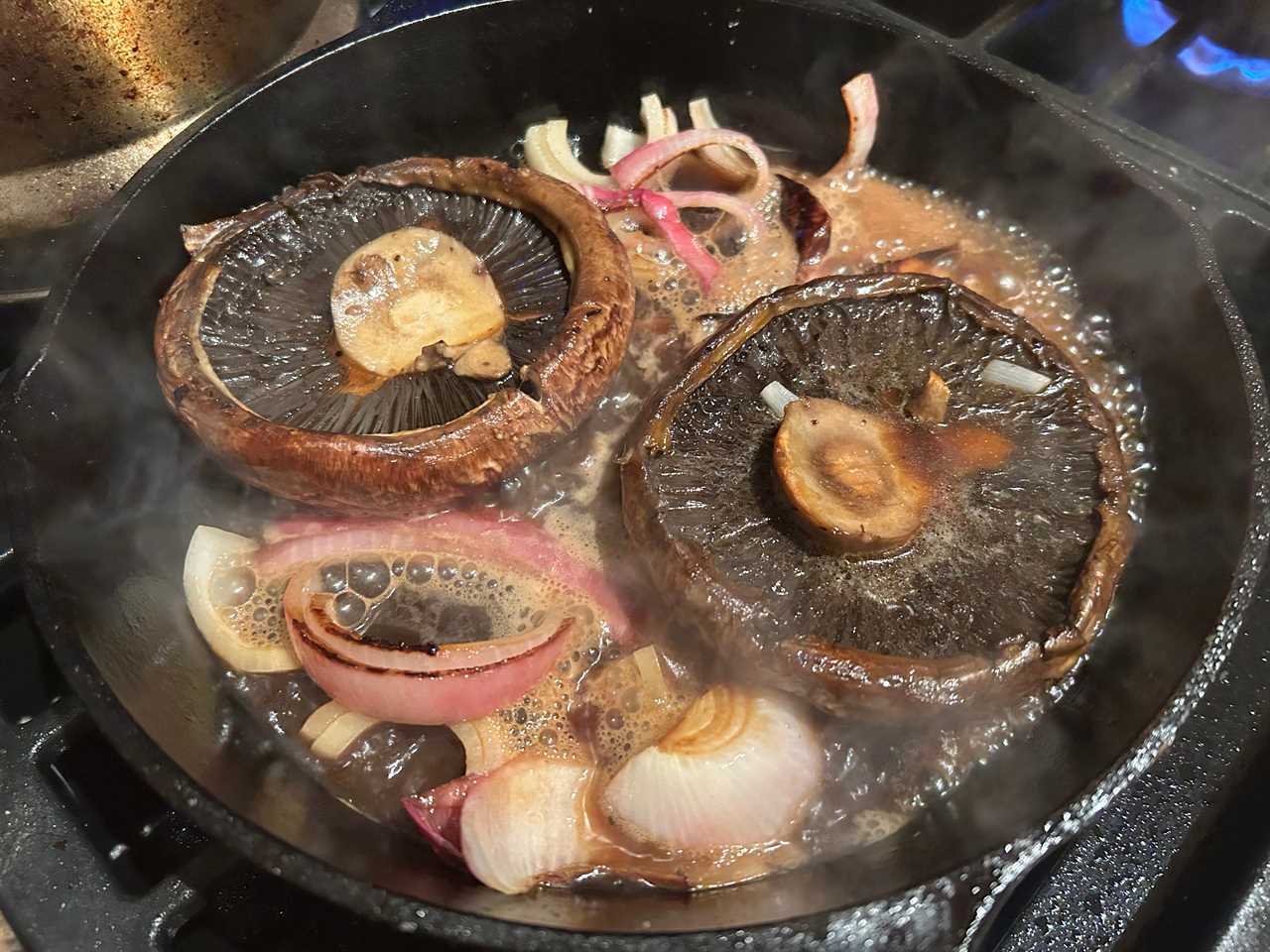 Portobello mushrooms and thick-cut onion slices cooking in a skillet on the stove.