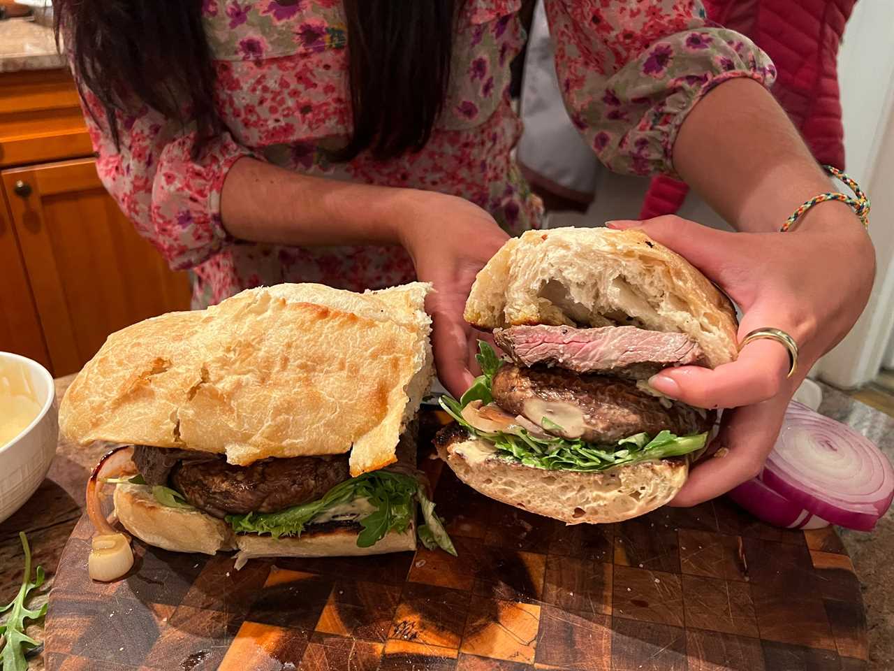 Lara's hands hold half of the steak sandwich up while the other rests on the cutting board.