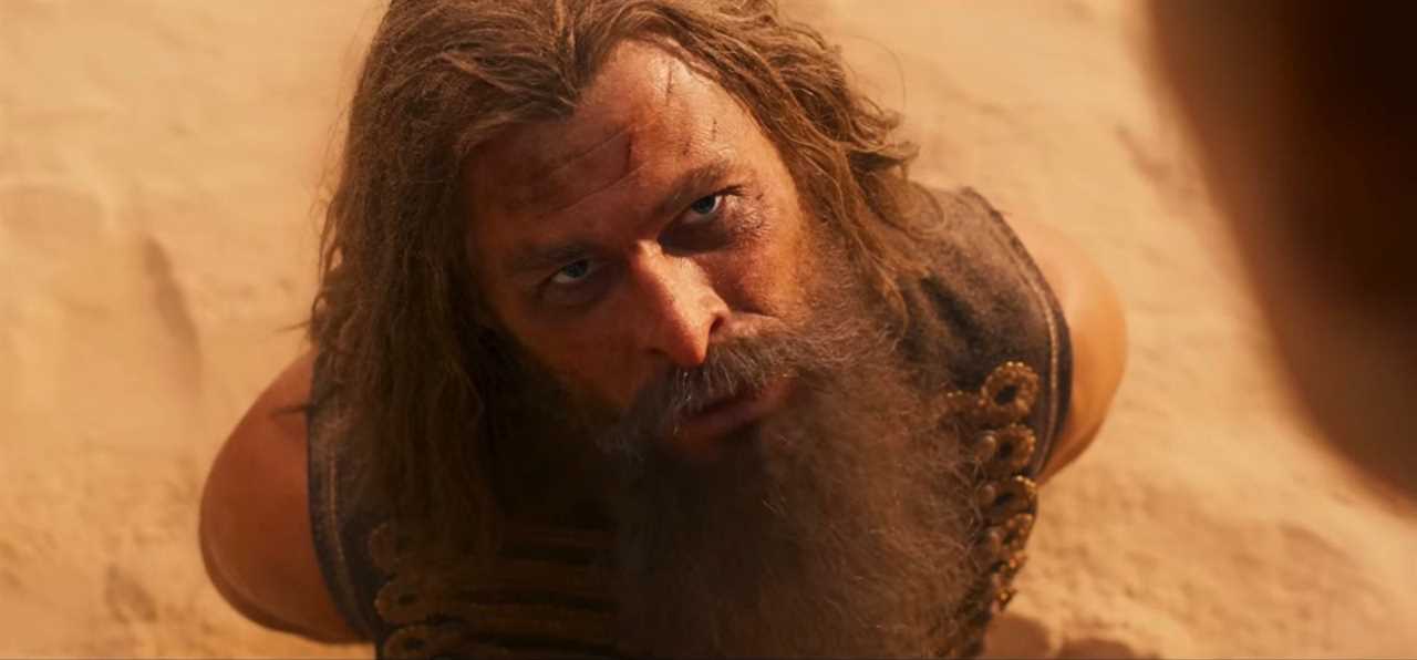 Chris Hemsworth in a beard kneeling in the sand