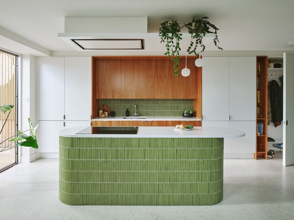 The new kitchen features green kit kat tiles, a terrazzo-effect rubber floor, white cabinetry, and cherry wood veneered cabinets. The client originally wanted teak cabinets, but 4 S Architecture recommended using cherry wood instead as it is more sustainable but has the same warm tones as teak. 