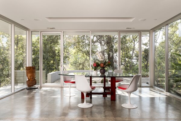 Floor-to-ceiling glass windows and doors encompass the dining area, framing striking views of the surrounding trees and canyons beyond.