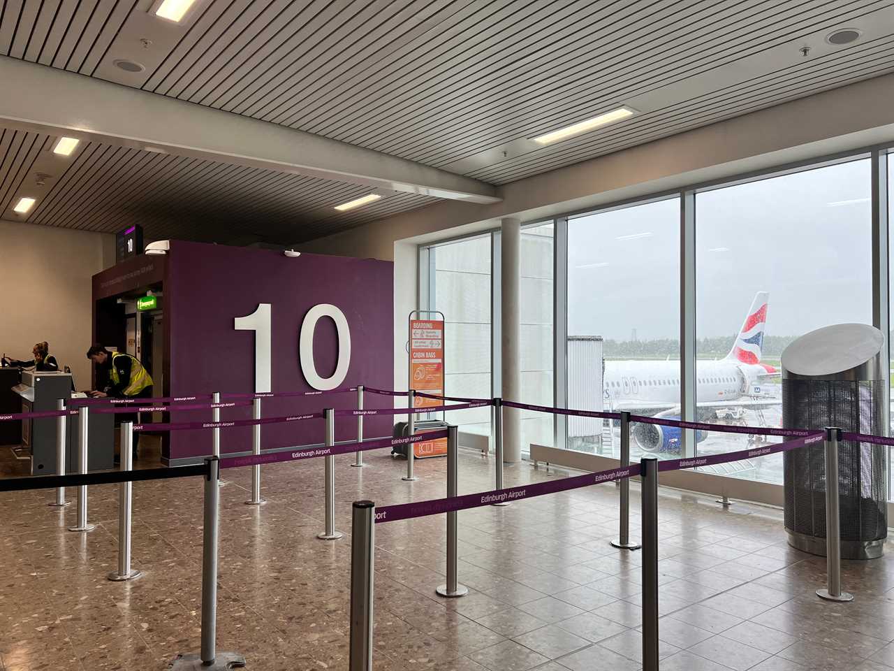 Gate 10 at Edinburgh Airport sees an empty queue and a British Airways Airbus A320 visible through th ewindow.