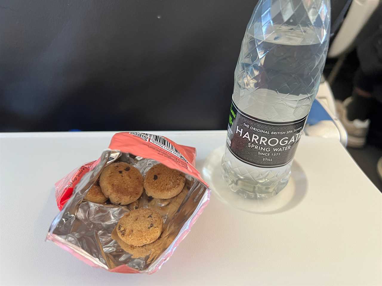 A small bag of cookies and a bottle of water on an airplane tray table