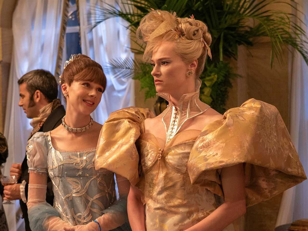 eloise standing next to cressida cowper in bridgerton, among a crowd in a ballroom. eloise is wearing a blue gown and smiling, while cressida looks forward, wearing an ornate gold gown