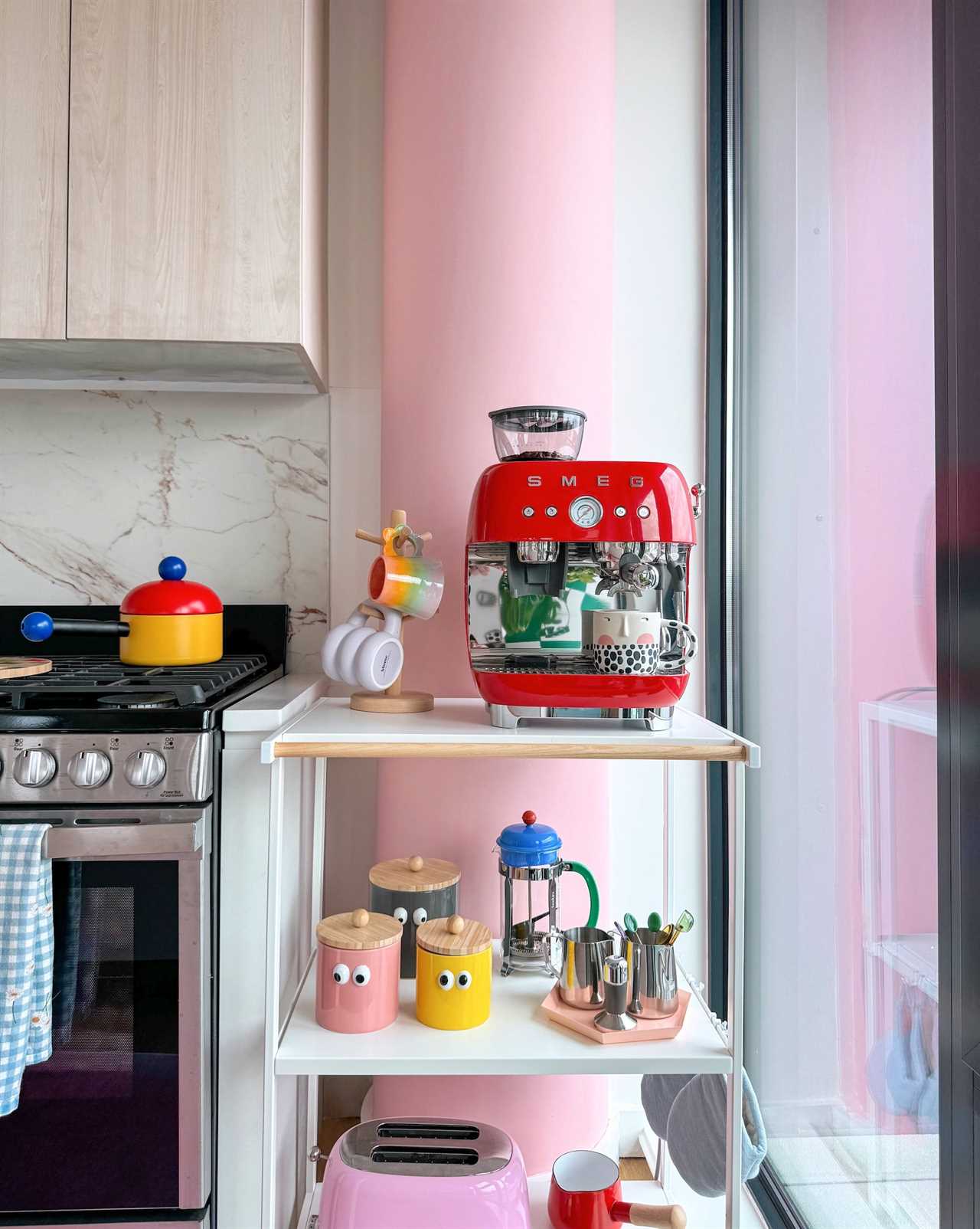 A shelf in a kitchen with colorful knick-knacks in front of a pink pillar.