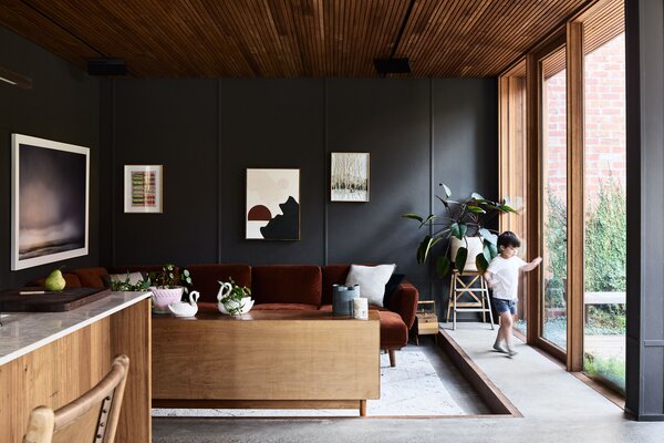 Project architect Chris Gilbert and Miranda Louey’s five-year-old, Arthur, balances on a custom couch from King Living in their townhome’s sunken living area on the ground floor. The couple wanted the units’ interiors to evoke the feeling of the bush where they grew up, so they went with Australian hardwoods for the joinery, including silvertop ash for the slatted ceilings throughout.