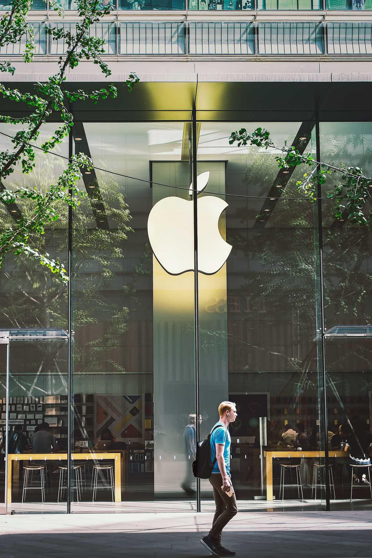 pedestrian walks past the Apple Store with reflection of branches in the glass