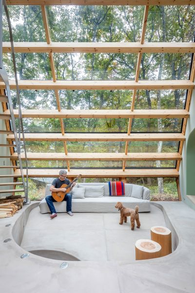 The living area is backed by sheer glass supported by wood beams. Here and in the side wings of the house, glazing tilts inward near the floor, making the volumes appear to float.