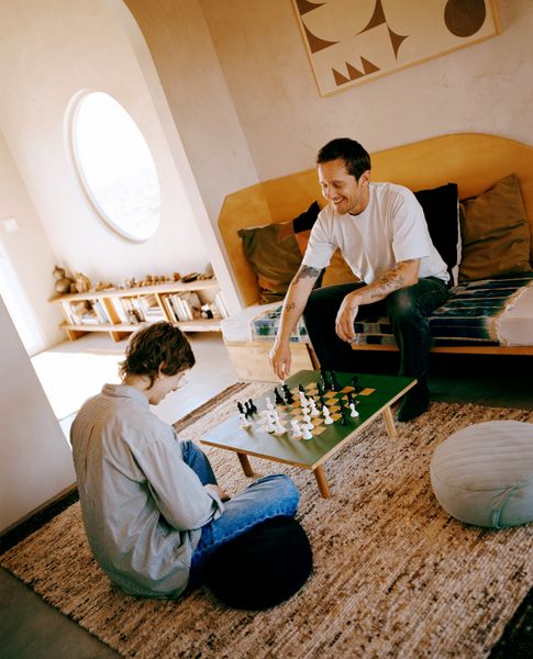 Artist Aaron Glasson and a friend relax in the 1950s Joshua Tree–area homestead cabin he and fellow artist Prescott McCarthy turned into a part-time home and artist residency. Aaron made the daybed, chess table, and artwork on the wall.