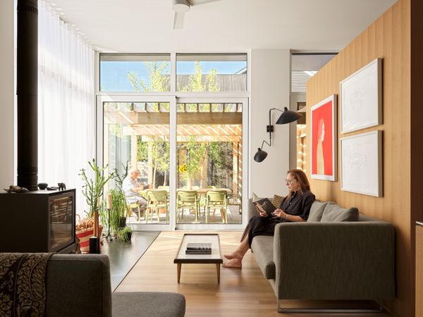 Tall ceilings and large windows and glass doors from Division 8 help fill the rooms with light. A red portrait by Shelley Adler and a pair of drawings by Jean-Paul Kelly hang above the sofa. The Serge Mouille 2 Arm Rotating Sconce mounted next to the sliding glass door is from Hollace Cluny.