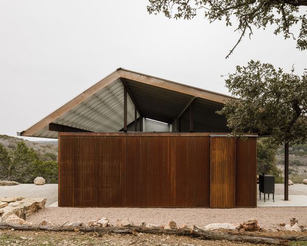 A workshop and storage space with corrugated metal siding sits at the northeast end of the house, adjacent to the carport. Deep roof overhangs provide shade during the hottest months.