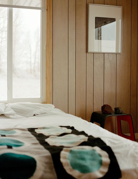 Surrounded by windows on three sides, a bedroom with wood-paneled walls retains vestiges of its sixties past and remains a work in progress. While debating the long-term layout of his now abode, Rael has made homey additions to his quarters, like a painted canvas in adobe by his partner, the artist Joanna Keane Lopez, found rocks, and one of three prints from Icy &amp; Sot, the multidisciplinary art practice of Iranian-born, Brooklyn-based brothers Saman and Sasan Oskouei.