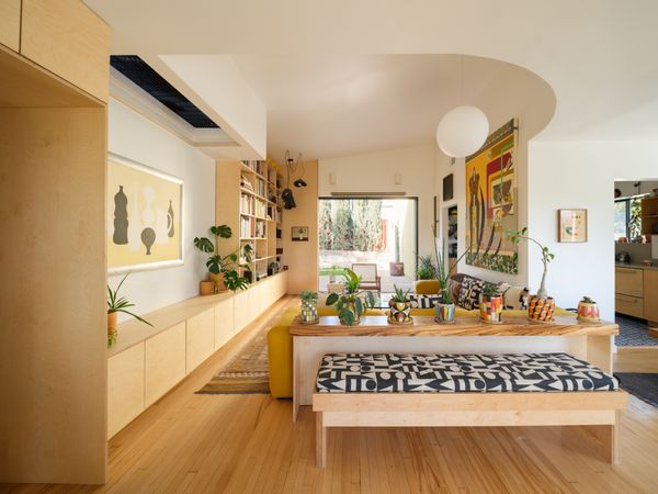 Displaying canvases by Steven Criqui (left) and Antonio Adriano Puleo (right), the transformed living room features a sculptural ceiling accented by a grate that brings light from the skylight in the expanded attic space above. Puleo designed the geometric print on the bench, which was made by James Melinat of Reigns Studio, who also built the custom cabinetry and bookshelves. Trifold sliders from Fleetwood open to the rear yard.