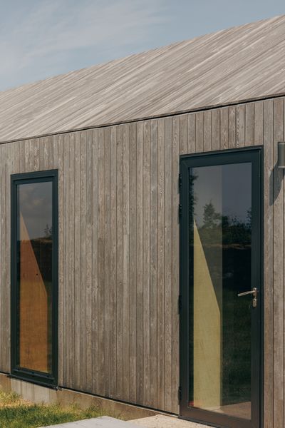 The black aluminum Senior Architectural Systems windows open flat to the Siberian larch exterior of the house. Guttering above the exterior walls is neatly concealed at the roof line.