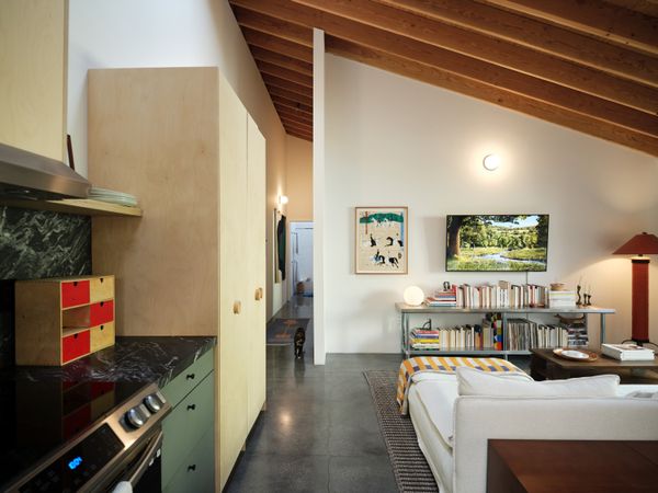 Hannah and Rami laid out the living area to face the television, which hangs above a restaurant-style metal shelving unit from Webstaurant. The sofa is an Ikea piece the couple had previously, and the rug is from West Elm. The floor lamp is another vintage piece.
