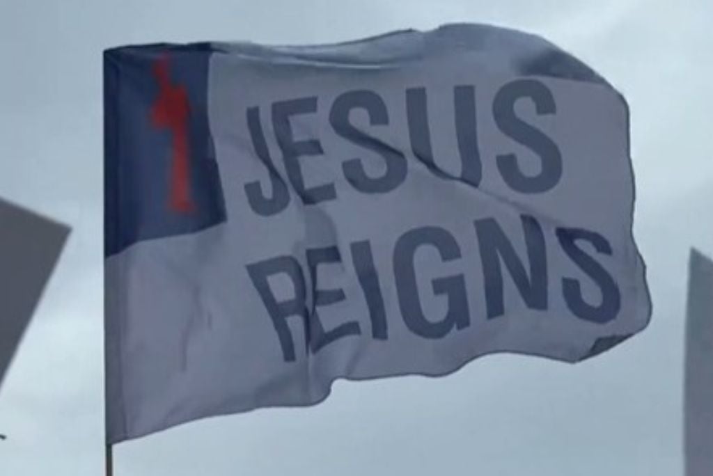 Flag displaying the message Jesus Reigns, symbolizing faith and religious expression at a public gathering.