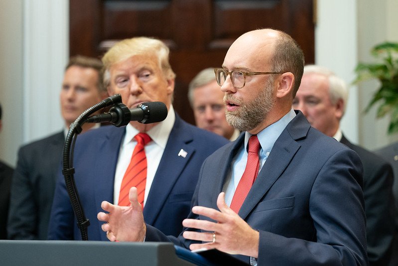 A speaker addresses an audience while Donald Trump listens attentively during a press event in the White House, highlighting key policy discussions.