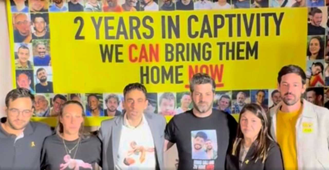 Group of activists standing in front of a banner advocating for the return of individuals held in captivity for two years, emphasizing urgency and support.