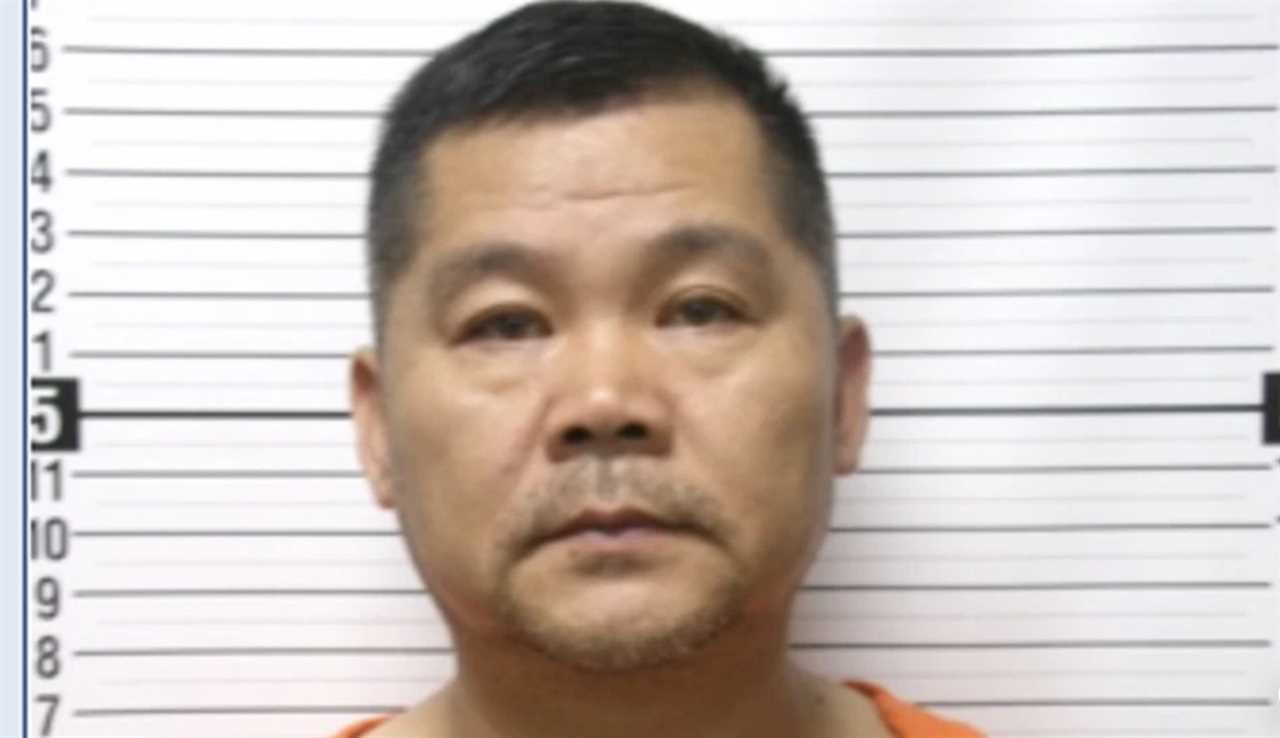 Mugshot of a man in an orange jumpsuit against a height chart background, showing a serious expression and short black hair.