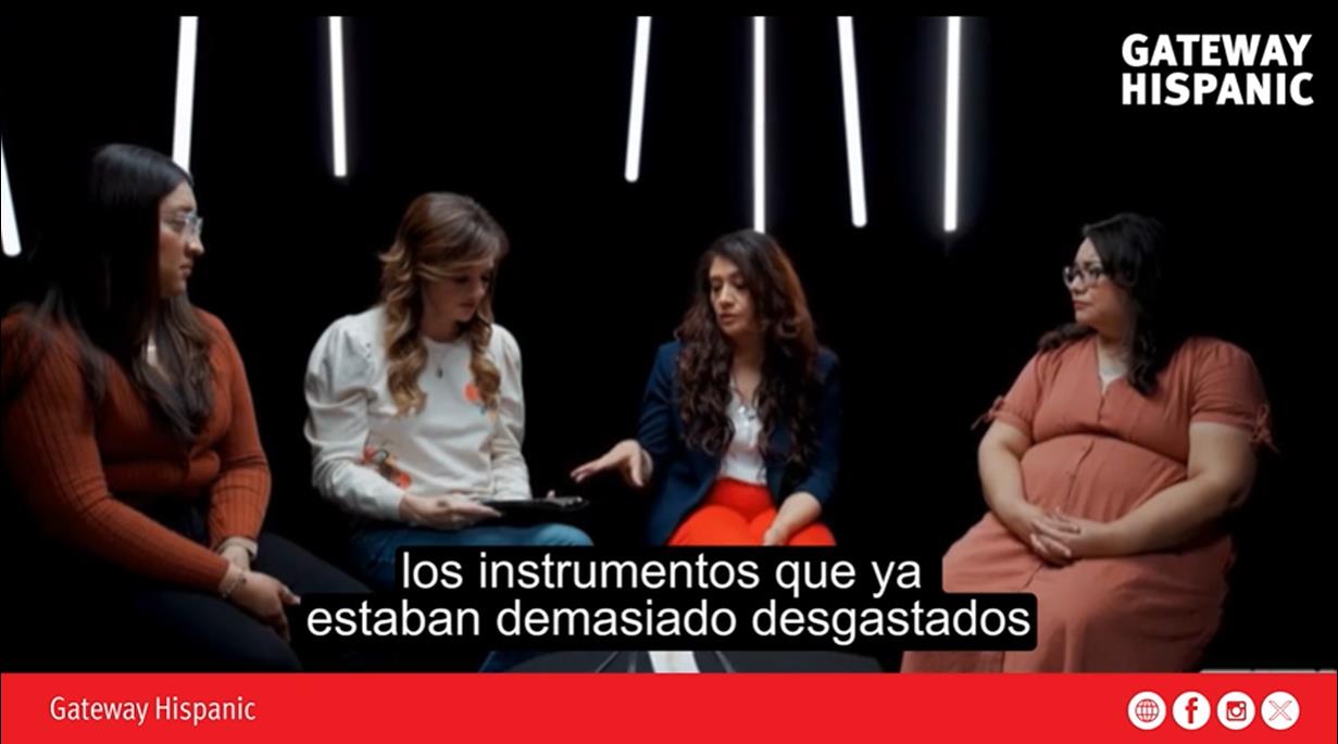 Four women engaged in a discussion about well-used instruments, set against a dark background with dramatic lighting.