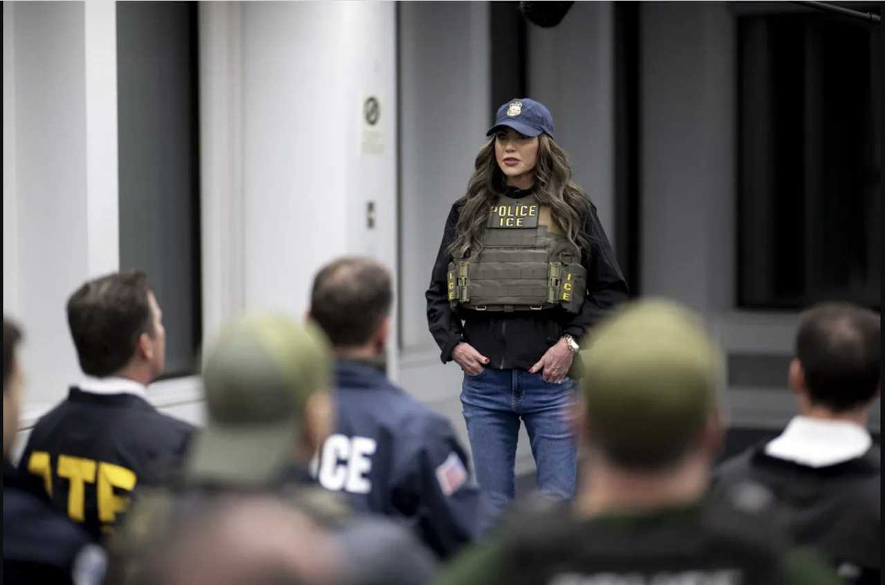 A law enforcement officer in tactical gear addresses a group of agents during a training session in a modern facility.