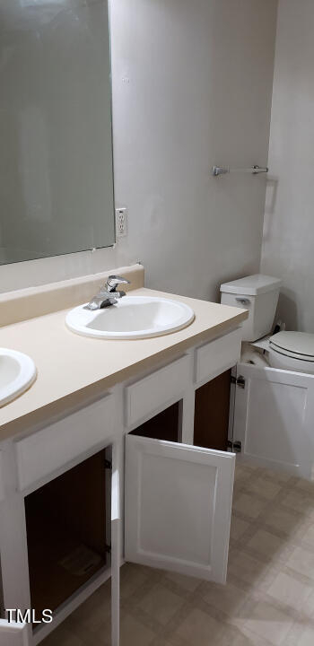 Outdated white bathroom with a mirror, two sinks a toilet and the cabinet doors open.