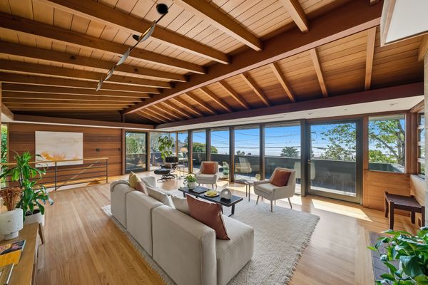 Floor-to-ceiling windows line the entire face of a living room wall, opening out to the second-story deck.