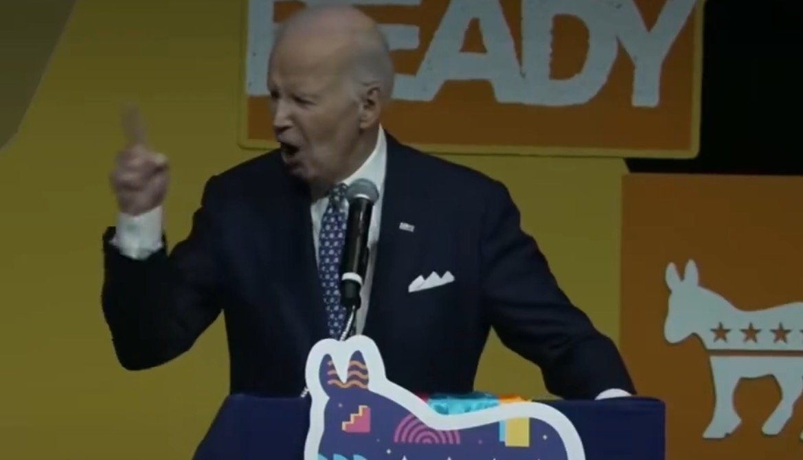Joe Biden passionately speaks at a podium during a political event, emphasizing key points with animated gestures against a vibrant backdrop.