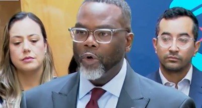 A man in a suit speaks at a press conference, flanked by two individuals, discussing important community issues.