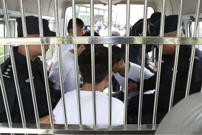 Police transporting detained individuals in a secured vehicle, with visible officers and a barred enclosure.
