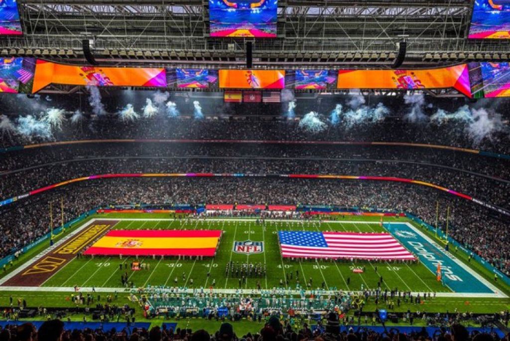 A vibrant NFL game scene featuring the Spanish and American flags, with a packed stadium and colorful displays overhead.