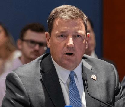 A man in a suit speaks at a congressional hearing, conveying important information with a serious expression and microphone in front of him.