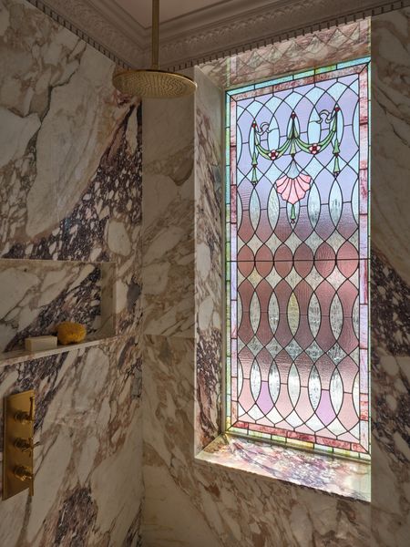 In the primary bathroom, defined by the pink stained glass window, the architect and her team painstakingly sourced slabs of Vagli Rosato pink and purple marble to wrap the walls around the shower and bathtub.