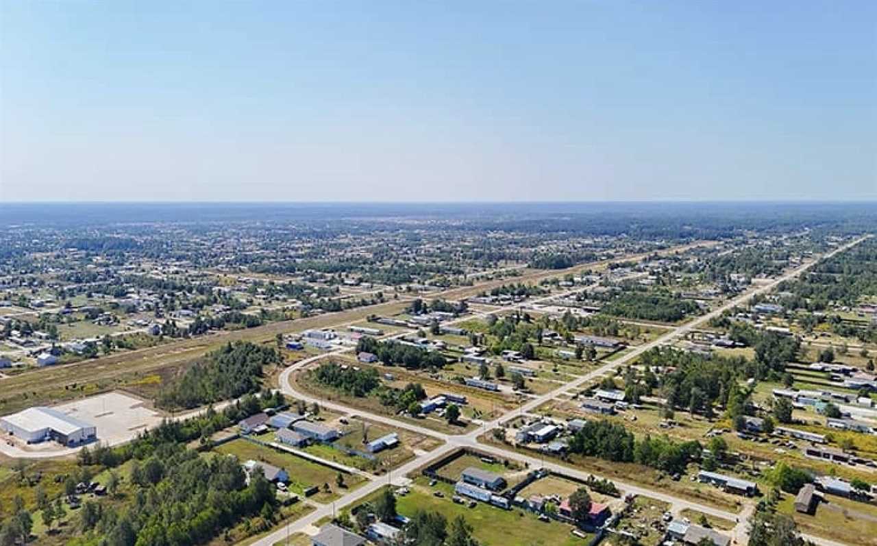 Aerial view of a suburban landscape featuring roads, homes, and green spaces under a clear blue sky.