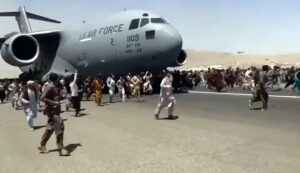 Crowd of people rushing towards a U.S. Air Force military cargo plane at an airport during a significant evacuation event.