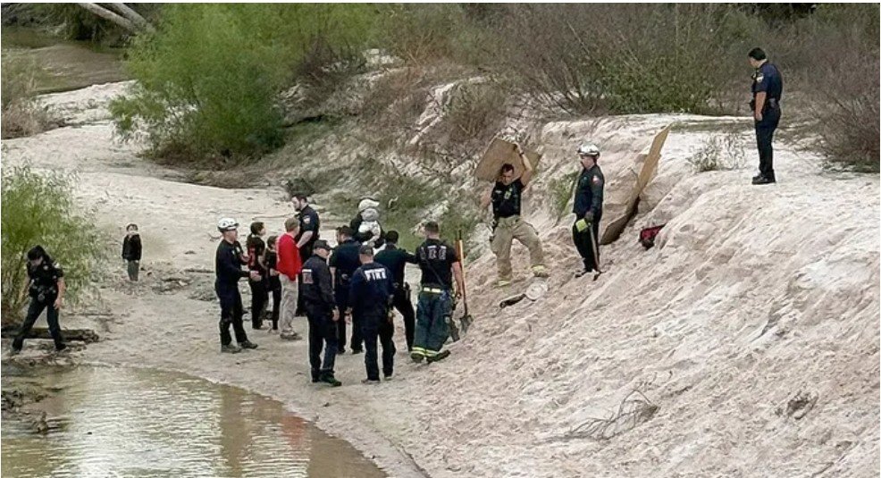 Emergency responders conducting a search and rescue operation along a riverbank, with several officials and a child in the background.