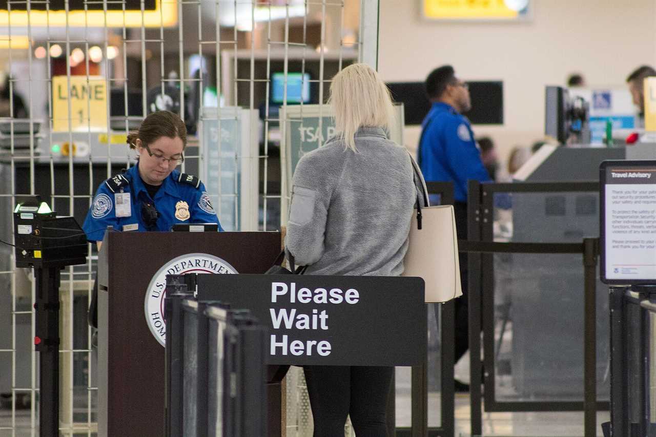 TSA officer assisting a traveler at airport security checkpoint with a sign indicating to wait in line.