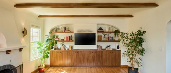 New custom cabinets and shelving, set into an arched recess, provide a place for storage, the TV, and display. The wood is the same black walnut as the shutters on the opposite side of the room.