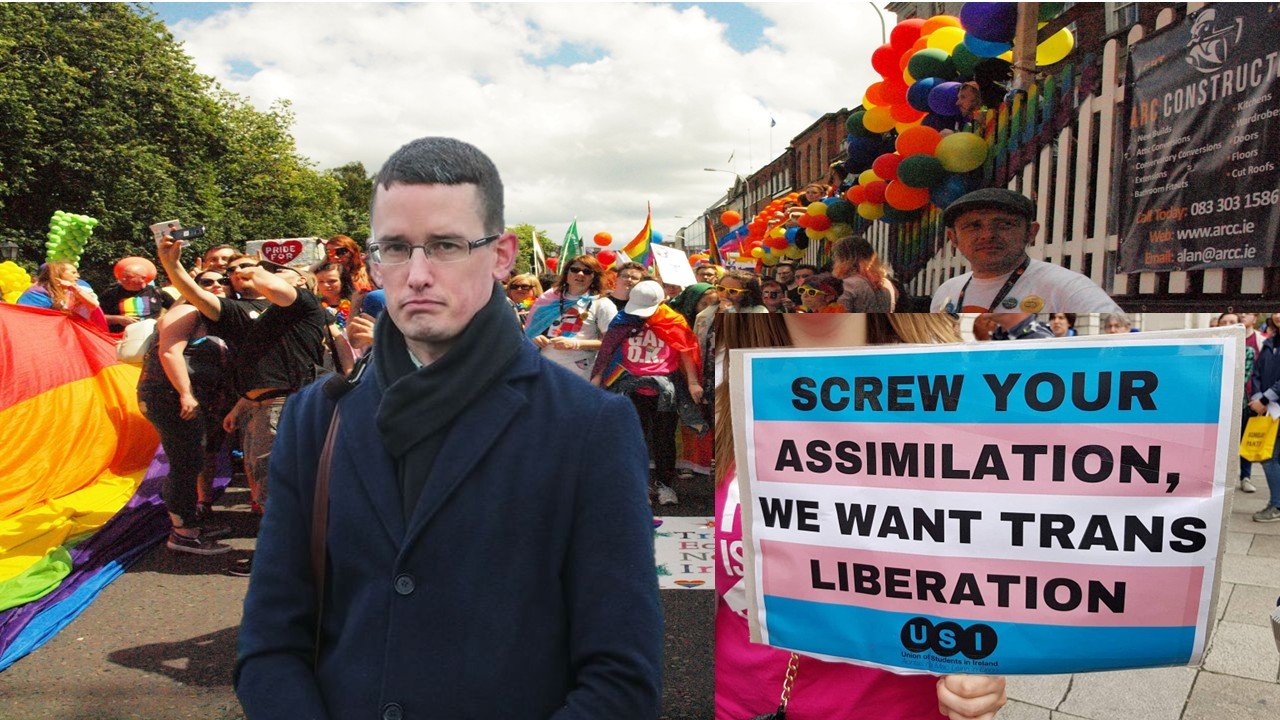 A person stands in front of a vibrant Pride parade, holding a sign advocating for trans liberation amidst a crowd celebrating LGBTQ+ rights.