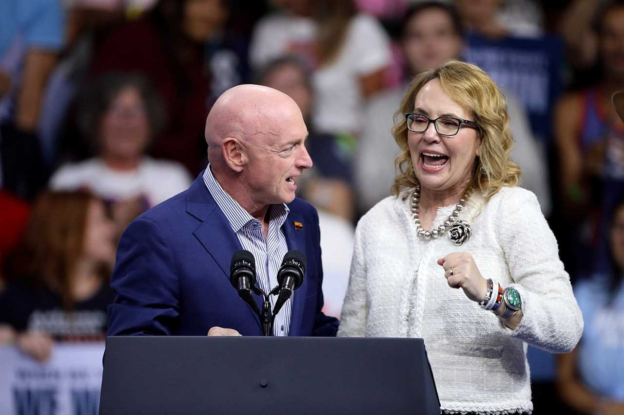 Two speakers engage enthusiastically at a political rally, with a cheering crowd in the background, highlighting a moment of excitement and connection.