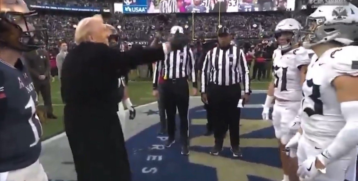 President Biden participates in the coin toss at a football game, surrounded by players and referees on the field.
