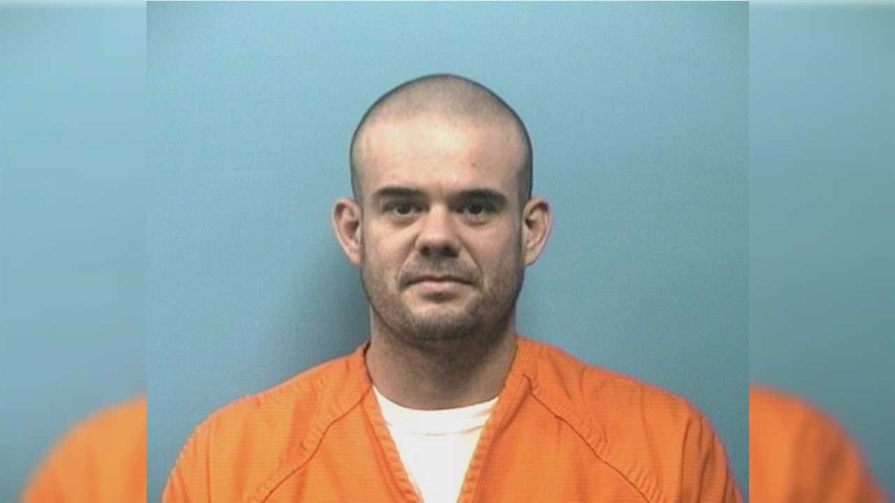 Mugshot of a man wearing an orange prison jumpsuit, with a neutral expression, against a blue background.