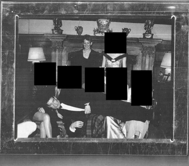 Black and white photo of a group of elegantly dressed individuals posing in a luxurious setting, with some faces obscured for privacy.