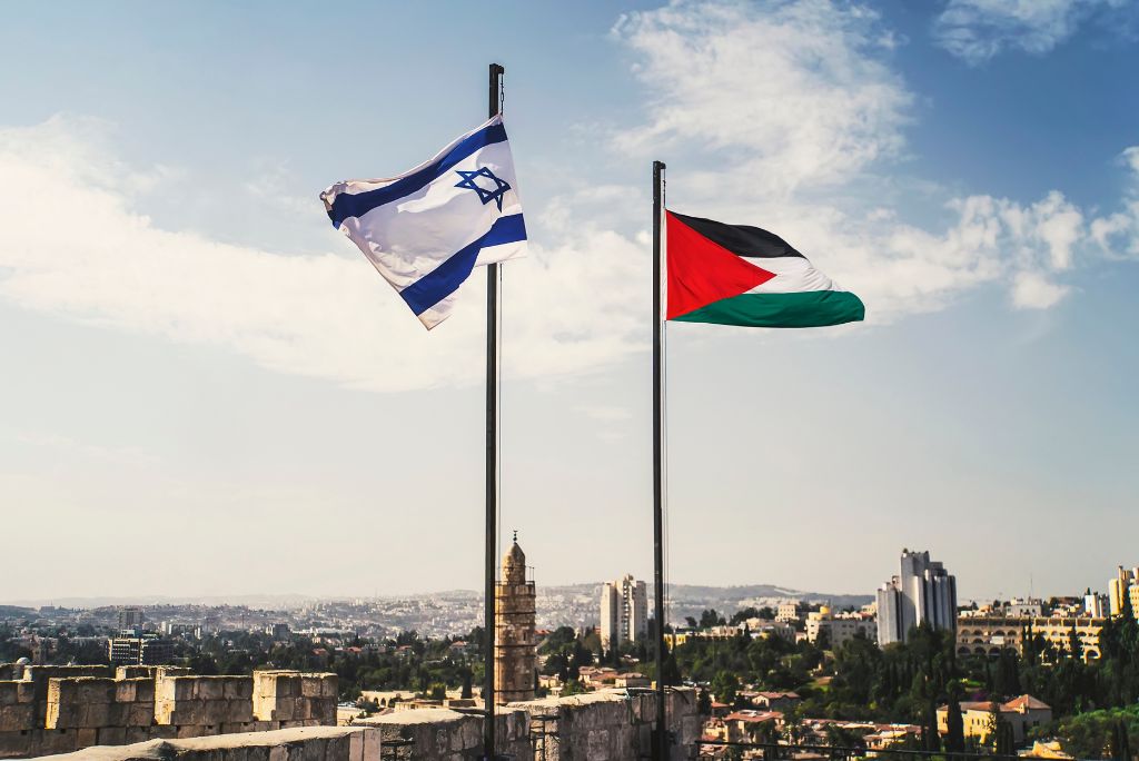 Israeli and Palestinian flags flying together against a backdrop of a city skyline, symbolizing the complex relationship between the two nations.