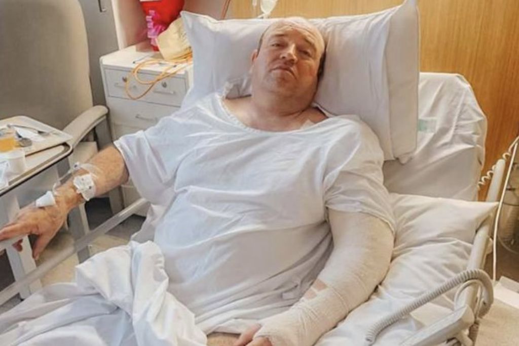 Patient in hospital bed wearing a medical gown with IV lines, showing signs of recovery after treatment, surrounded by hospital equipment.