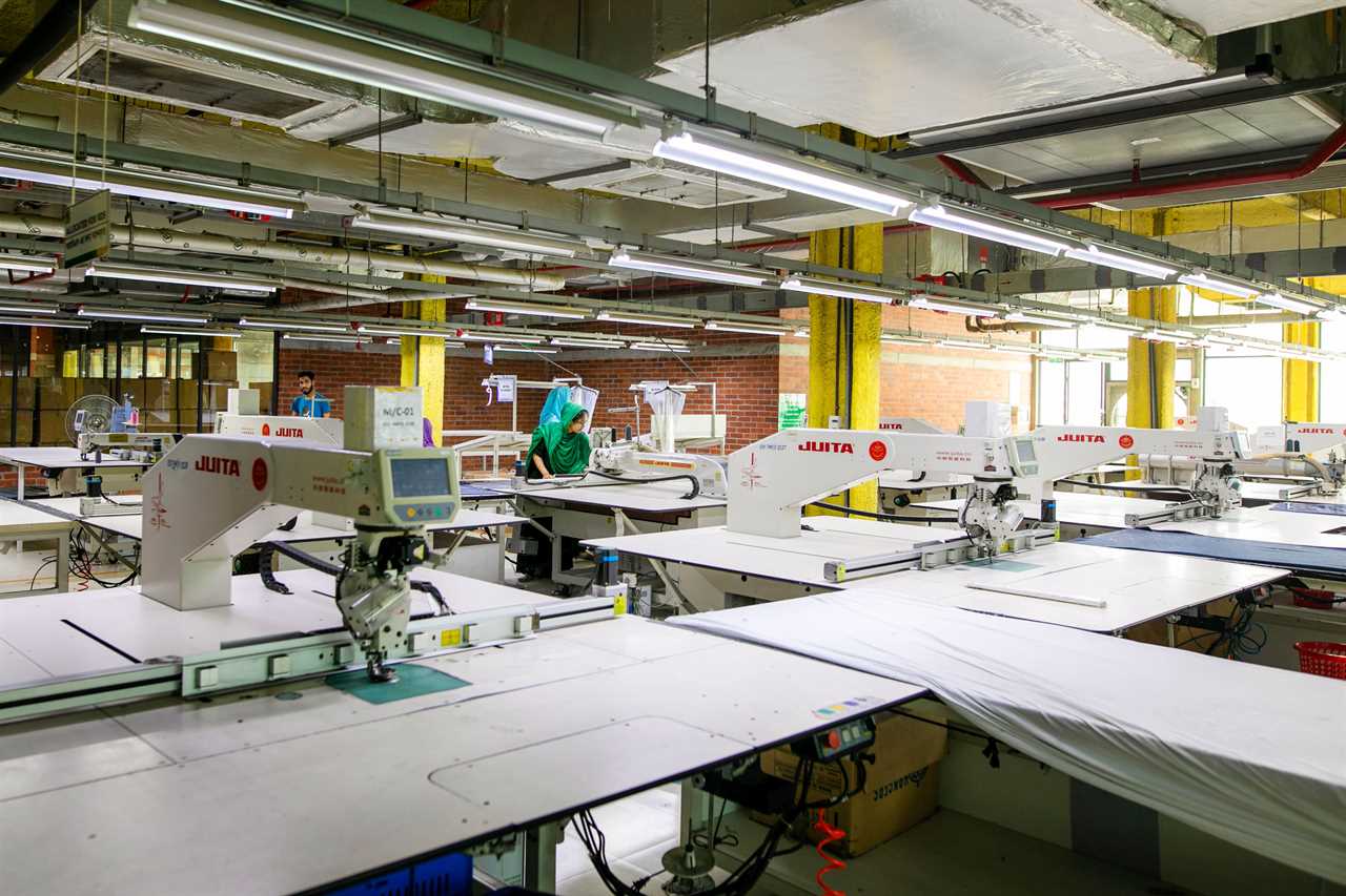 a single factory worker in the midst of many workstation tables under industrial lighting fixtures