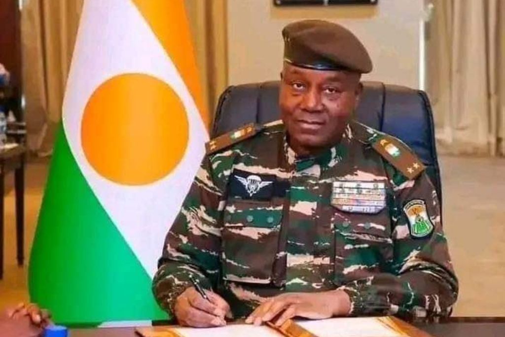 Military officer in camouflage uniform signing documents with Niger's flag in the background, representing leadership and governance.